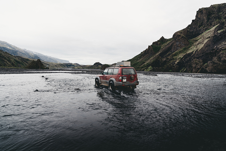 红色SUV在山附近的水上行驶