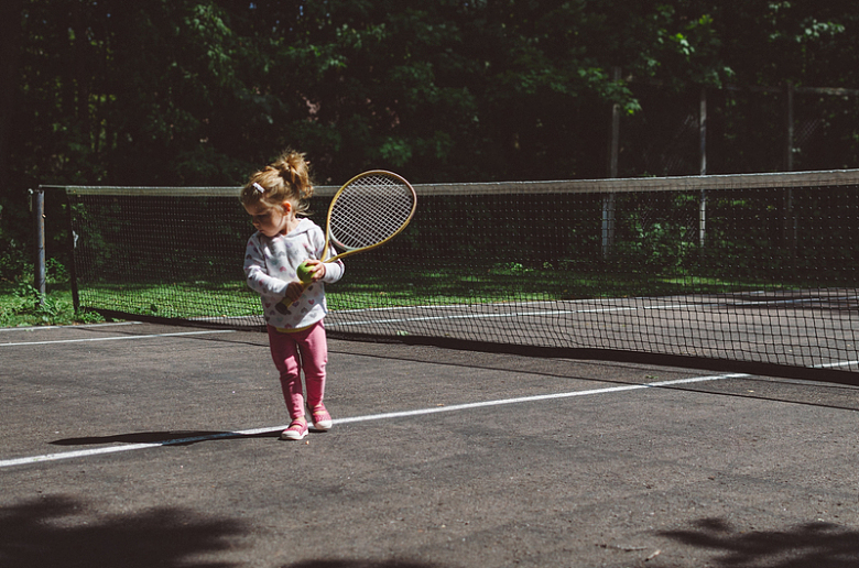 女孩拿着草坪网球拍站在黑白相间的网旁