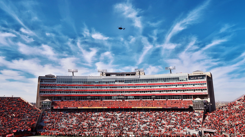 一群鸟在蓝天下飞越红白相间的体育场