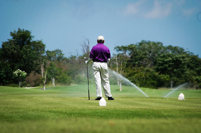 穿着紫色夹克和白色裤子的男子白天打高尔夫球