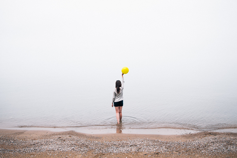 女生手举黄色气球在海滩上