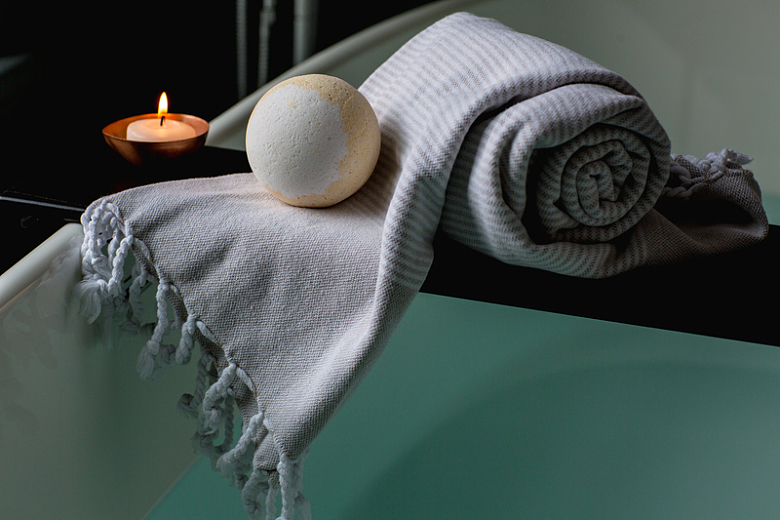 一卷毛巾和香薰蜡烛和浴缸炸弹在浴缸的木板上