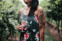 一名身穿碎花裙子手拿葡萄酒纹身刺青女性站在葡萄园内