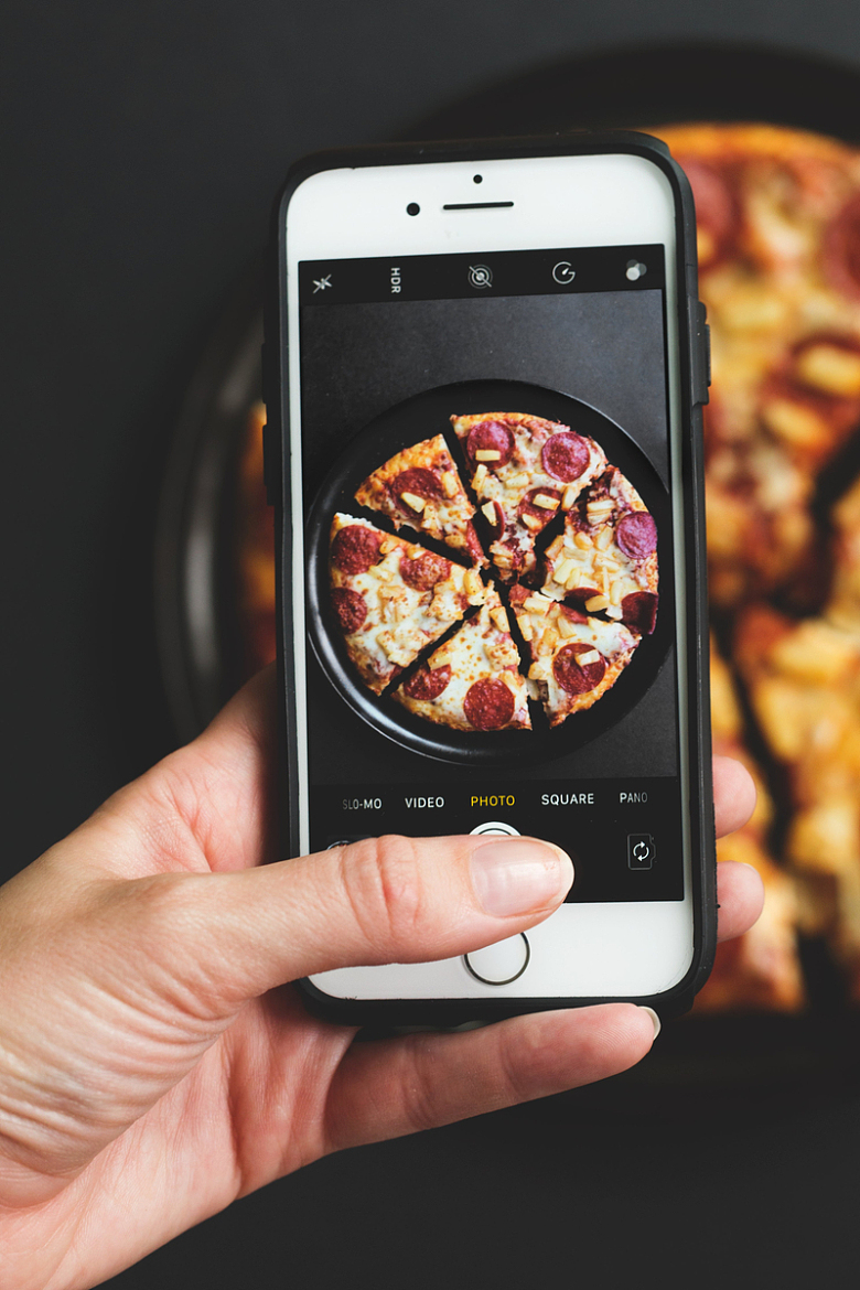 手拿手机拍照美食披萨