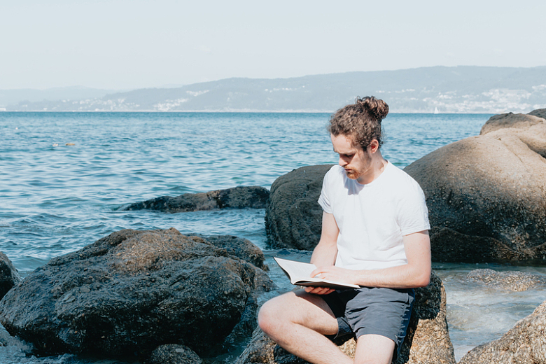 坐在海边的岩石上看书的男子