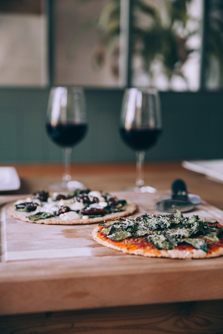 木板上的两个大披萨旁边放着几杯葡萄酒