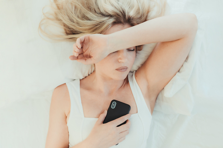 一个女人在床上举起一只胳膊拿着手机
