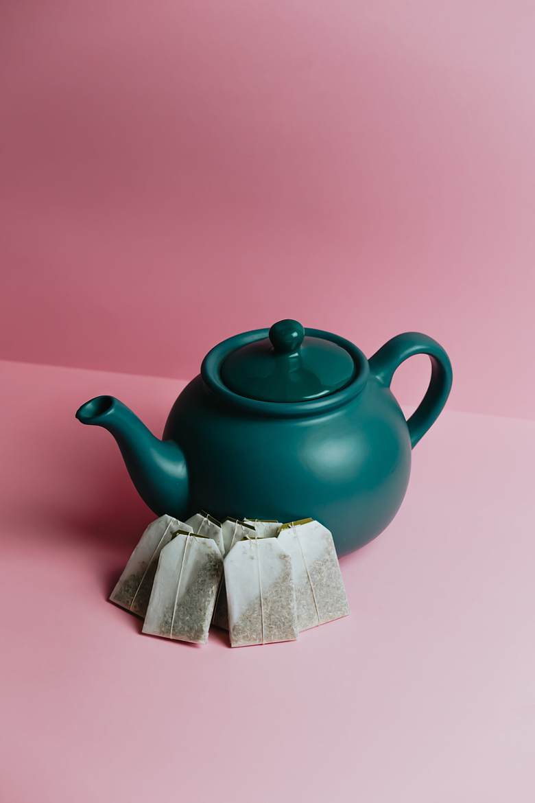 粉色背景上绿色的茶壶和茶包
