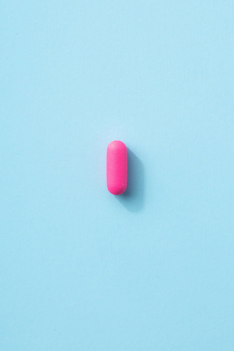 浅蓝色桌面上的的粉红色药丸