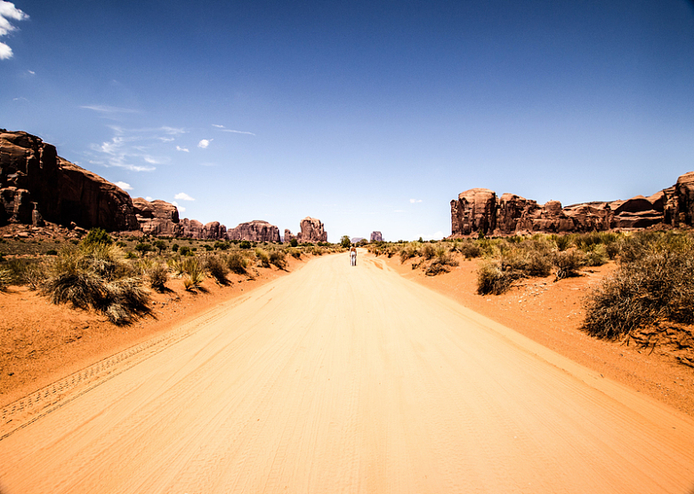 蓝天下一个人影站在沙漠中的一条路上